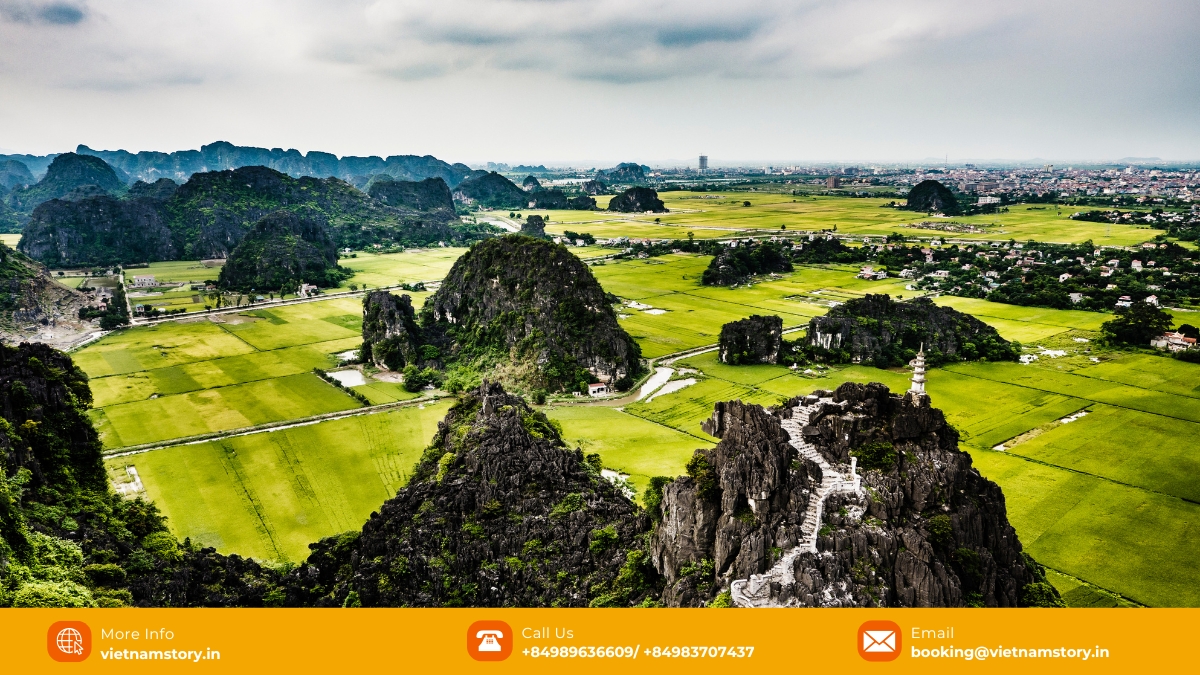 A traditional bamboo boat navigates the serene waters of Van Long Wetland Reserve, with golden rice paddies and towering limestone cliffs in the background.